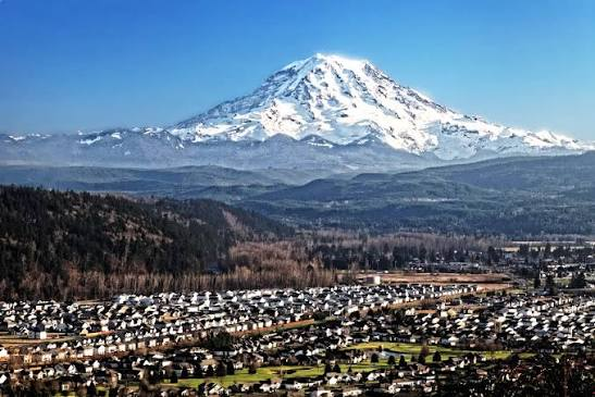 Snow-capped Mount Rainier rising above forested foothills and a small town under a clear blue sky